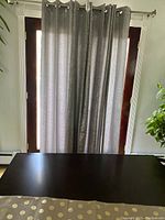 Photo showing a set of silver-colored drapes hanging on a rod in front of a glass door with light coming through, drapes have a shiny texture and grommet top.