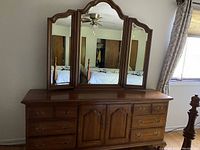 Photo of wooden dresser with trifold mirror, showing front view with drawers and cabinet doors.