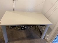 Photo of a rectangular light-colored desk with cylindrical metal legs, showing top, legs, and floor underneath with cables visible