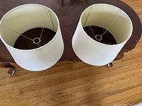Two white fabric lamp shades placed side-by-side on a wooden table, showing top and side views with visible metal spider frames inside.