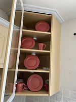 Cabinet shelf showing four pink salad plates and four matching mugs.