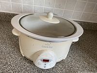 Cream-colored Crock-Pot slow cooker with glass lid and digital control panel on a kitchen counter.