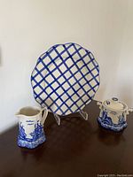 Photo of a decorative porcelain plate with blue lattice design and matching coffee pot and sugar bowl with blue scenic motifs.