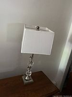 Photo of a table lamp with a stacked glass orb design and white rectangular shade standing on a wooden surface against a white wall.