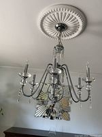 Photo of a silver metal chandelier with six arms, crystal drops, candle-style light bulbs, and decorative ceiling medallion.