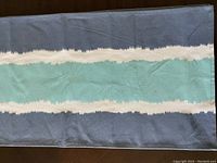 Photo of fabric table runner laid flat showing horizontal stripes in grey, white, teal, white, and grey pattern.