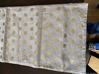 Top view of white or light-colored table runner with gold polka dots spread out on a floor surface