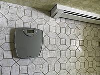 Gray digital bathroom scale on tiled floor with digital display visible