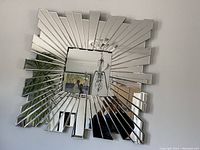 Square 3D wall mirror with radiating rectangular mirrored panels in a modern geometric design.