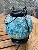 Close-up photo showing the globe-shaped candle holder made of crackled blue glass with black metal handle.