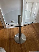 Round clear glass top and metal pedestal base table shown from an angle to see overall design.