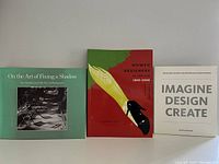 Three books against a plain wall: 'On the Art of Fixing a Shadow', 'Women Designers in the USA 1900-2000', and 'Imagine Design Create'.
