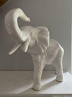 Front and side view of white glossy ceramic elephant statue with trunk raised.
