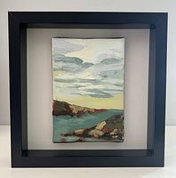 Black square shadowbox frame with mounted oil painting inside, depicting rocky coastline and cloudy sky.