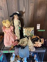 Two porcelain dolls, cloth‐body doll and assorted clothing on shelving