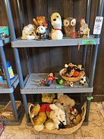 Three-tier shelving unit with ceramic banks on top shelf, small toys on middle shelf, plush on bottom shelf