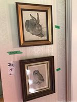 Two framed wildlife prints hanging on wall, one featuring a hare and the other an owl, each with visible price tags and measurement stickers