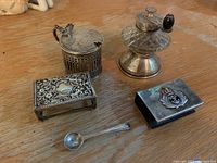 Photo showing all silver items together on wooden surface including salt cellar, pepper grinder, matchbox cover, spoon, and another small holder