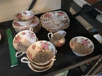 Full set of porcelain tea cups, saucers, cream pitcher, and sugar bowl with pink floral design and some gold trim.