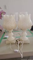 Pair of cream white marble accent lamps with carved floral/petal design. Visible cords with inline switches. Lamps have solid base blocks and sculpted shades standing about 12 inches tall.
