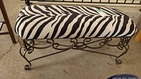 Full view of padded bench showing zebra pattern upholstery and decorative cast iron base with scrollwork design.