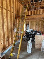 Full view of the 28-foot yellow extension ladder standing upright inside a wooden frame structure with other items visible in the background.