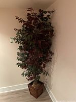 Full view of the faux plant with red and green leaves in the wooden square pot placed in a corner.