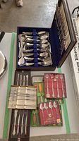 Full view of Pfeiffer flatware in blue velvet-lined wooden canteen case, additional boxed silverware sets and butter spreaders on table