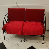 Full front view of the bench showing red seat and back cushions on black iron frame