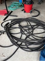 Coiled heavy duty black garden hose on concrete floor with a red shop vacuum and some other tools nearby.
