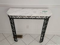 Front view of marble hall table with metal frame against wall and tiled floor.