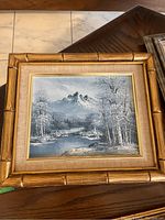 Framed original mountain scene painting on a table showing the entire frame and painting details.