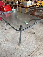 Front angled view of rectangular glass top patio table with black metal frame and umbrella hole in center.