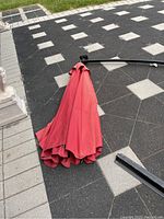 Folded red umbrella canopy and detached frame legs laid on patterned pavement