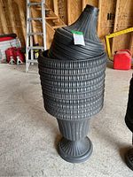 Stacked black plastic plant pots with ribbed texture, mounted on matching pedestal stands.