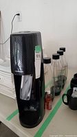 Front and side views of the black SodaStream soda maker with four clear bottles behind it