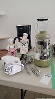 Overview of all items on table including coffee percolator, hand mixer, and two chef figurines