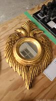 Carved gold painted wood frame with small round mirror and feather motif, on wooden surface