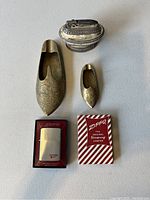 Photo showing two vintage Japanese shoe ashtrays, one antique lighter, one brand new Zippo lighter in box, and a decorative silver-toned ashtray.