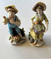 Photo of two decorative statues, a boy holding a duck and a girl carrying a basket of produce, showing detailed painting and craftsmanship.