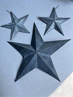 Three decorative metal stars of different sizes placed on a light surface, showing texture and hooks for the small stars.
