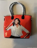 Front view of the purse featuring an image of Michelle Obama against a red background with handles wrapped in plastic.