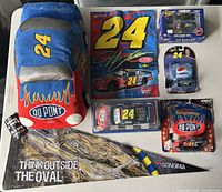 Photo showing all lot items arranged on a table including plush car, multiple boxed diecast cars, autographed banner, and Sonoma flag.