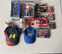 Photo showing all 11 NASCAR collectible items arranged on a flat surface including the boxed Terry Labonte figure, NASCAR ornament in packaging, two Jeff Gordon caps, two boxes of playing cards, and multiple racing souvenir cards