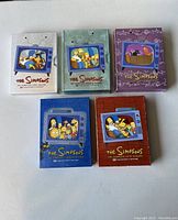 Five DVD cases of The Simpsons seasons 1-5 arranged on a white surface, each with distinct colorful cover art.