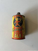 Photo shows a cylindrical vintage Esslingers Premium Ale beer can with a yellow and red painted design featuring a cartoon man holding a beer mug and surface rust.