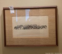 Full photo of framed artwork showing a herd of elephants walking in a line across a light background in a wood frame.