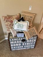 Storage bench with six decorative pillows stacked on top, featuring a variety of designs including floral and message prints.