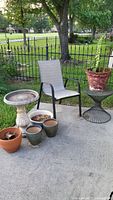 Photo showing the outdoor bird bath, five various sized plant pots, one patio chair, and part of metal garden table outdoors