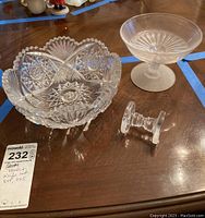 Cut glass decorative bowl, glass footed bowl, and glass cutter rest grouped on table.